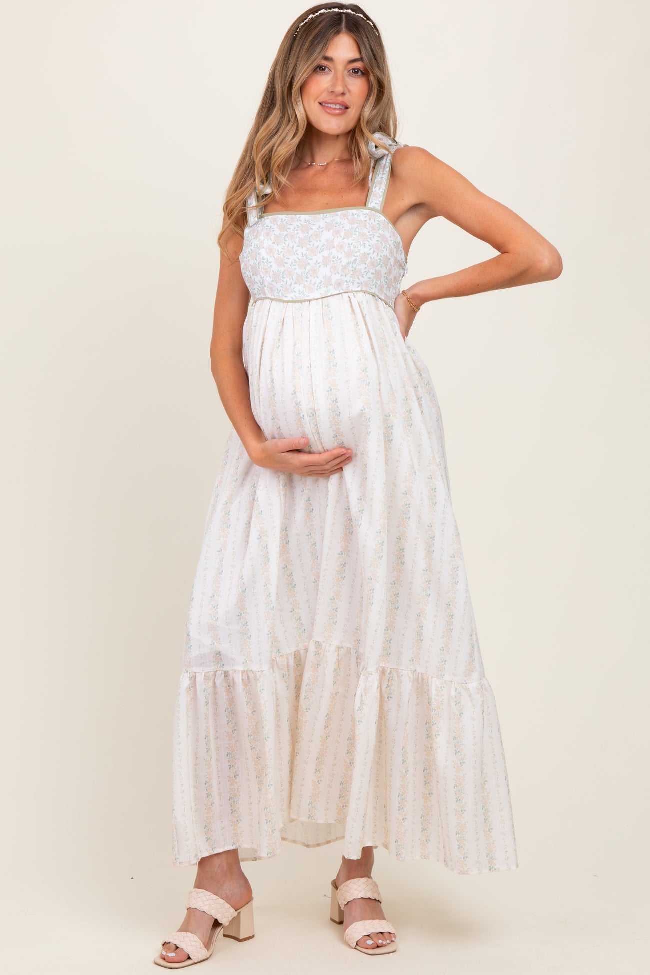 woman wearing a floral print maternity maxi dress with tied straps and holding her baby bump