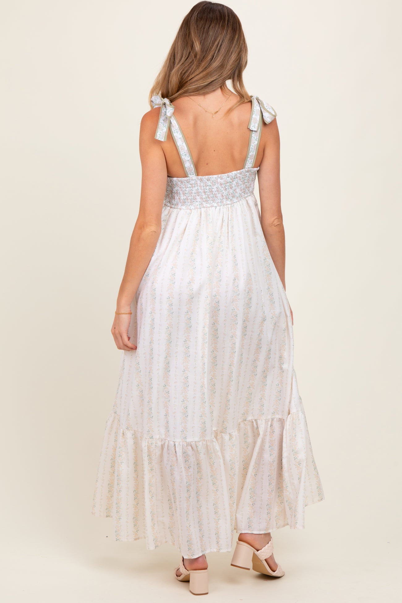 woman wearing a cream and blue floral print maternity maxi dress with tie straps and a smocked back