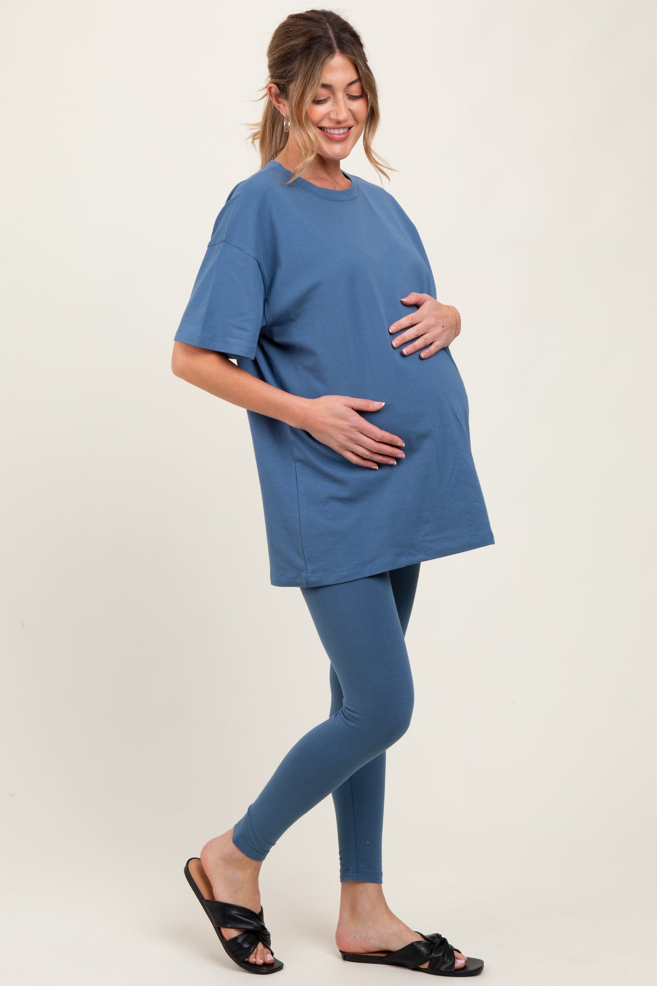 woman wearing a blue oversized maternity t-shirt and blue leggings, gently holding her baby bump