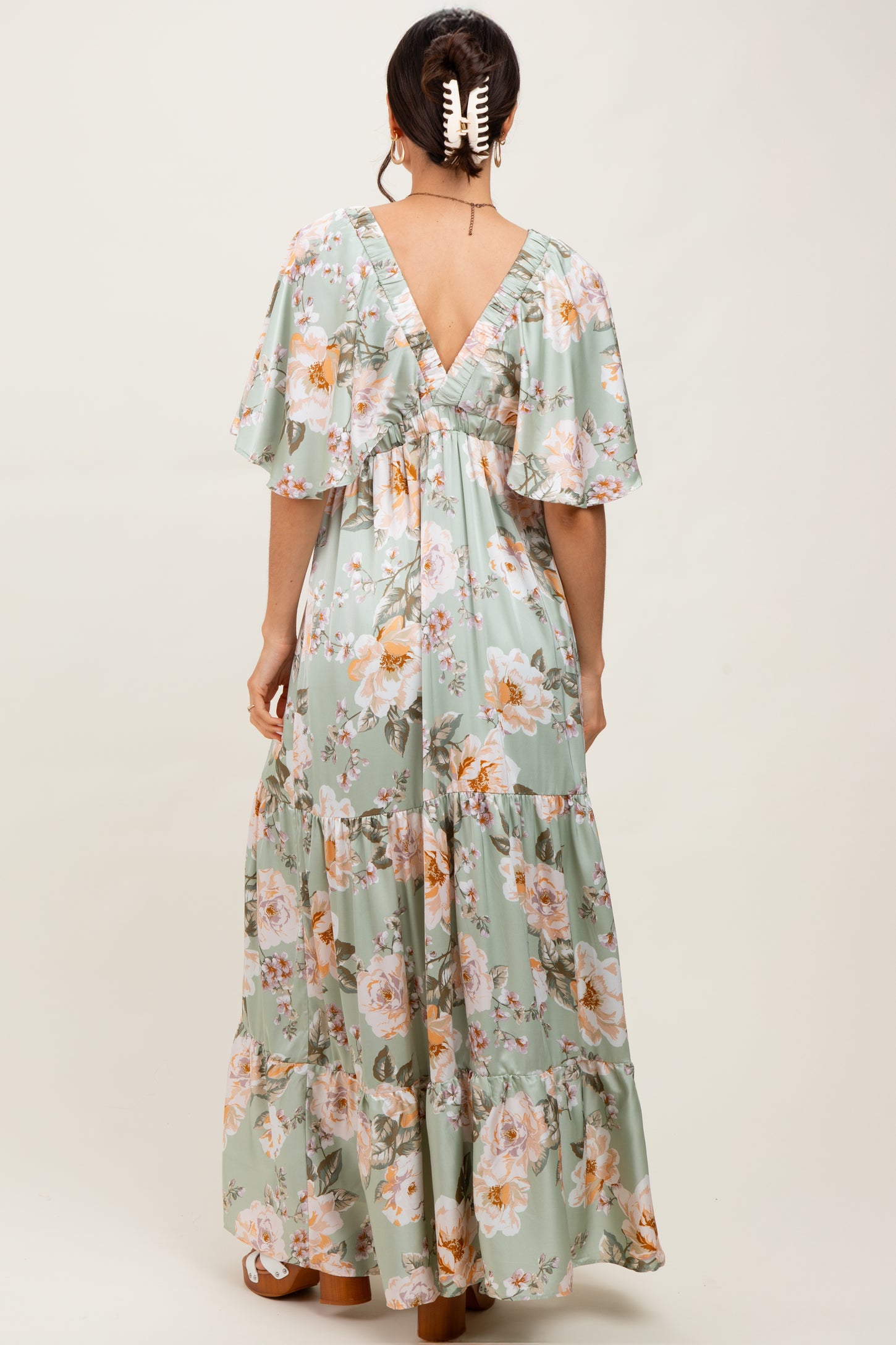 woman wearing a light green floral maxi dress with flutter sleeves and a v-back design