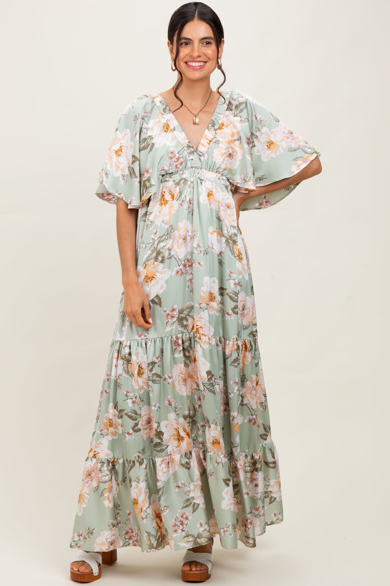 woman wearing a green floral maxi dress with flutter sleeves and a tiered skirt
