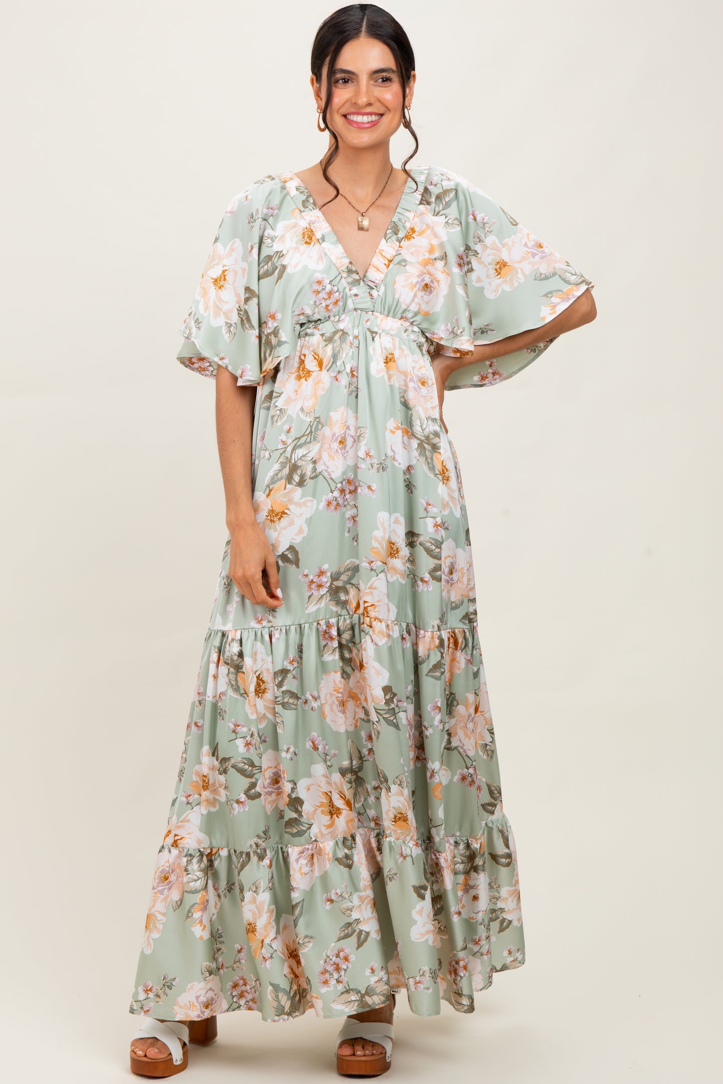 woman wearing a green floral maxi dress with flutter sleeves and a tiered skirt
