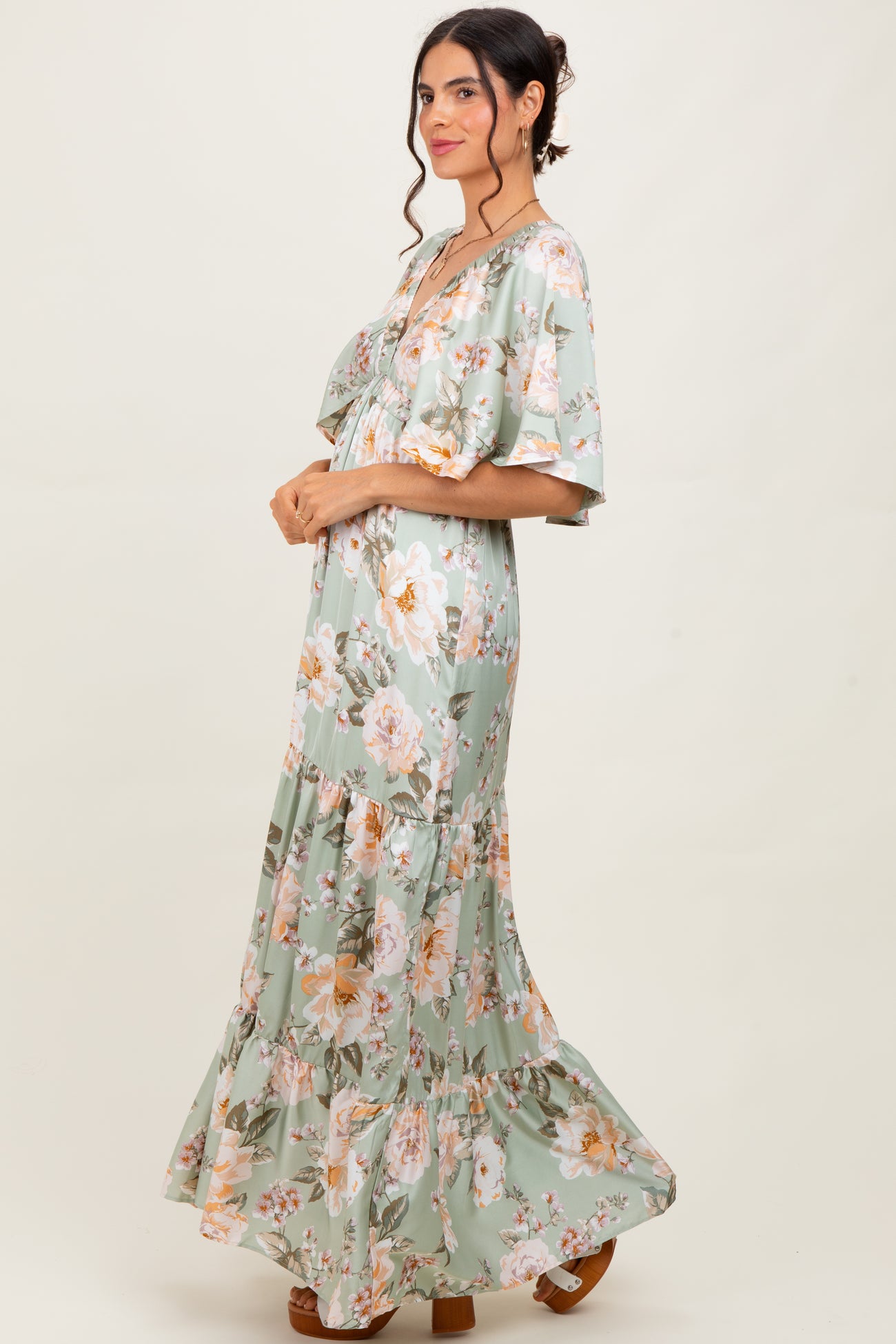 woman wearing a light green floral maxi dress with short flutter sleeves and a tiered skirt