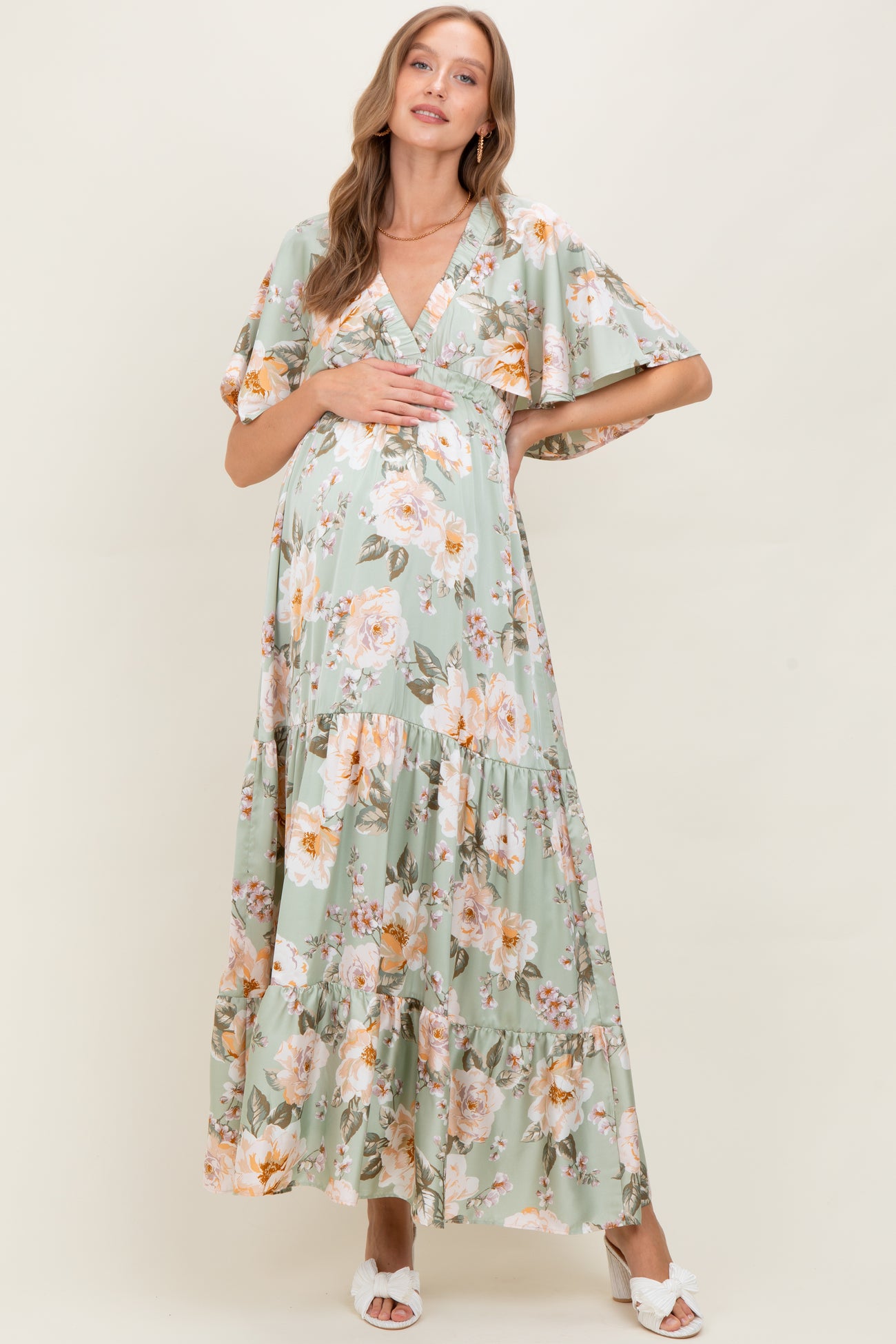 woman wearing a floral print green maternity maxi dress and holding her baby bump