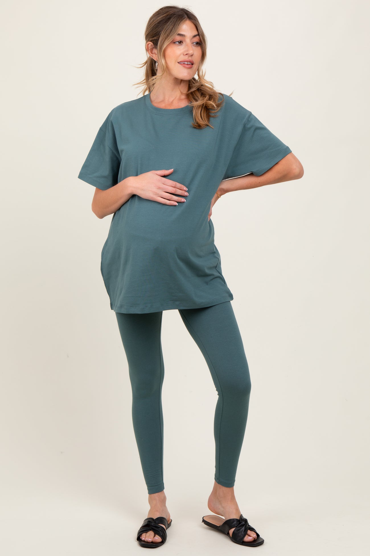 woman wearing a teal maternity top and matching leggings, holding her baby bump