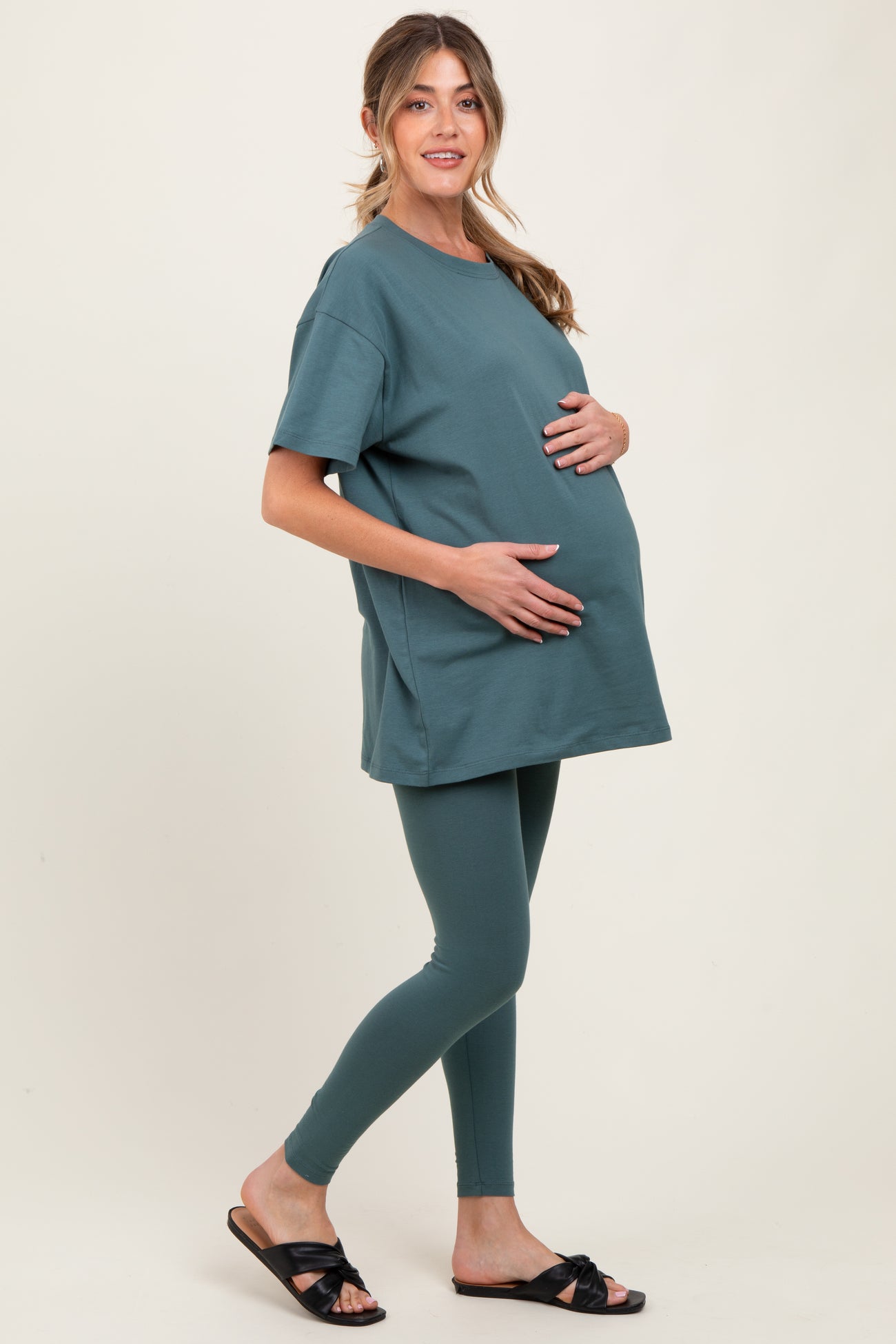 woman wearing a teal oversized maternity t-shirt and matching leggings, holding her baby bump