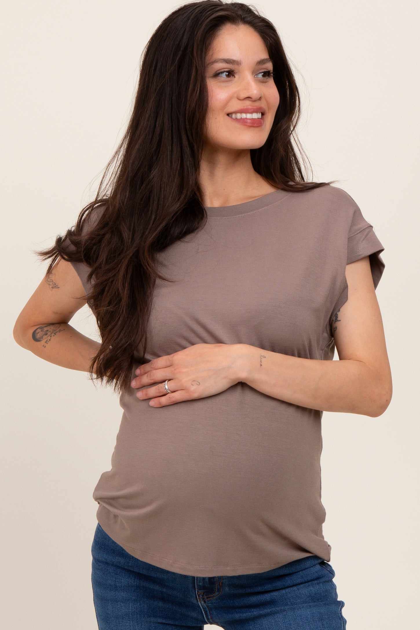 woman wearing a taupe maternity top and gently holding her baby bump