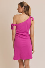 woman wearing a fuchsia one-shoulder dress with tie detail on the shoulder, showing the back view