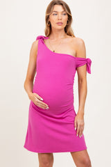 woman wearing a hot pink one-shoulder maternity dress with tie details and holding her baby bump