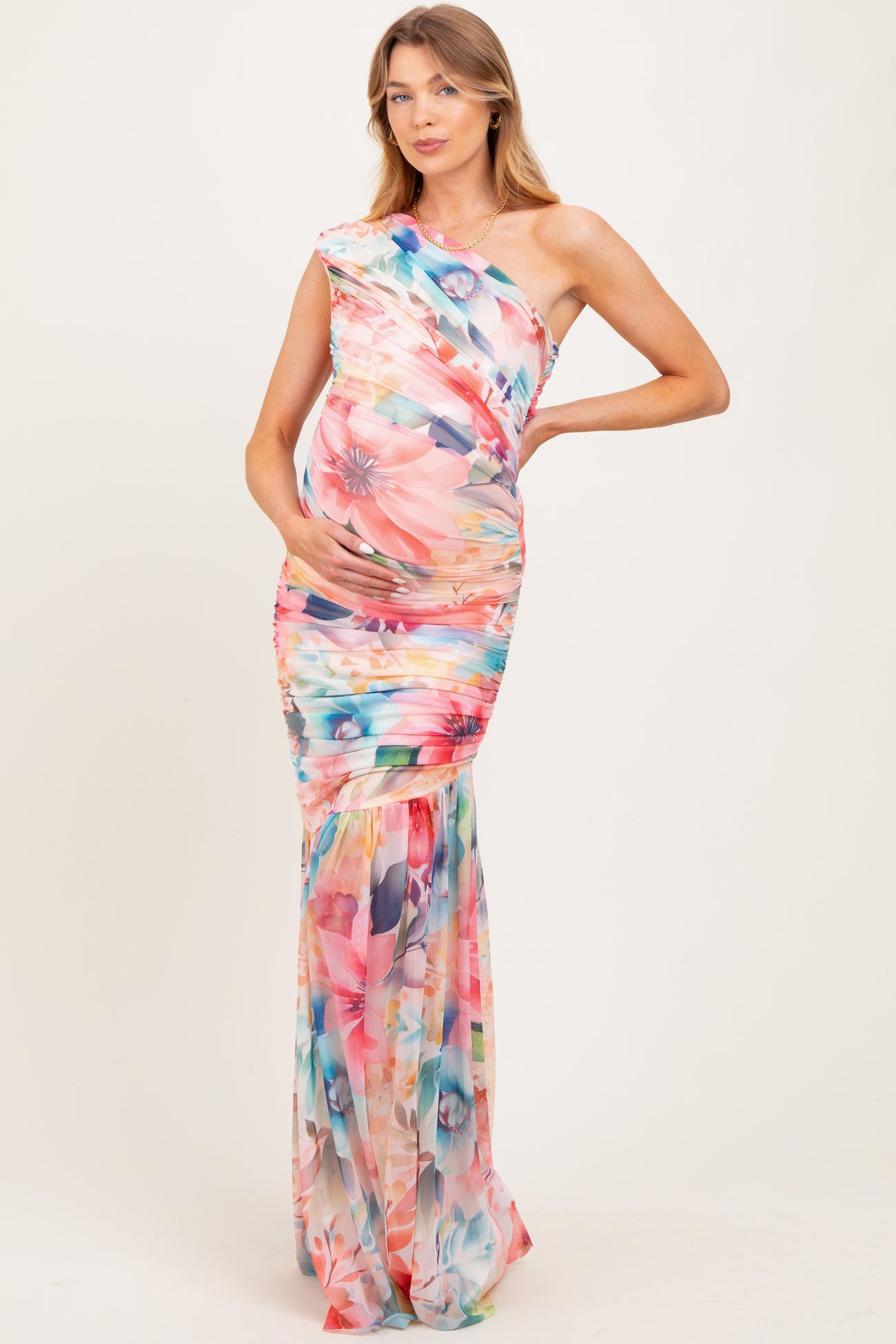 woman wearing a floral one-shoulder maternity gown, showcasing her baby bump and a fitted silhouette