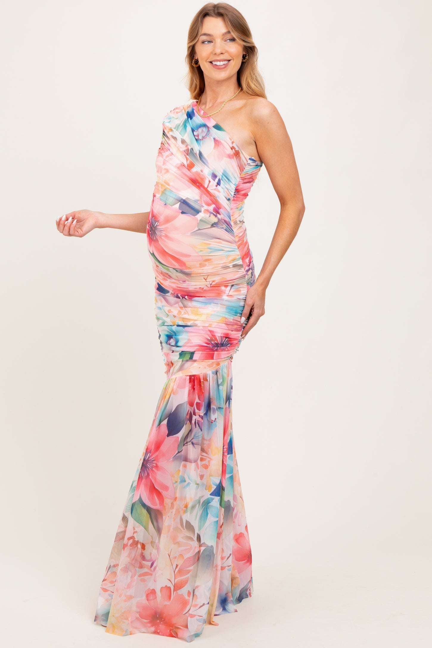woman wearing a colorful floral one-shoulder maternity gown with a fitted bodice and flowing skirt, showcasing her baby bump