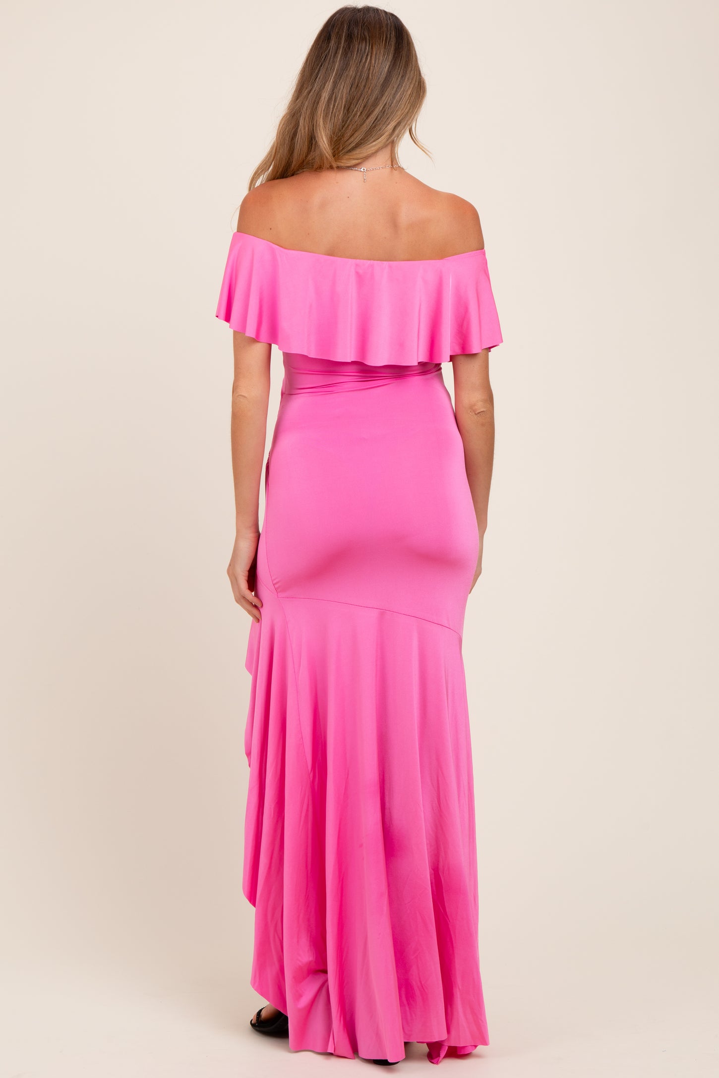 woman wearing a pink off-the-shoulder maternity dress with a ruffled bodice and flowing skirt from behind