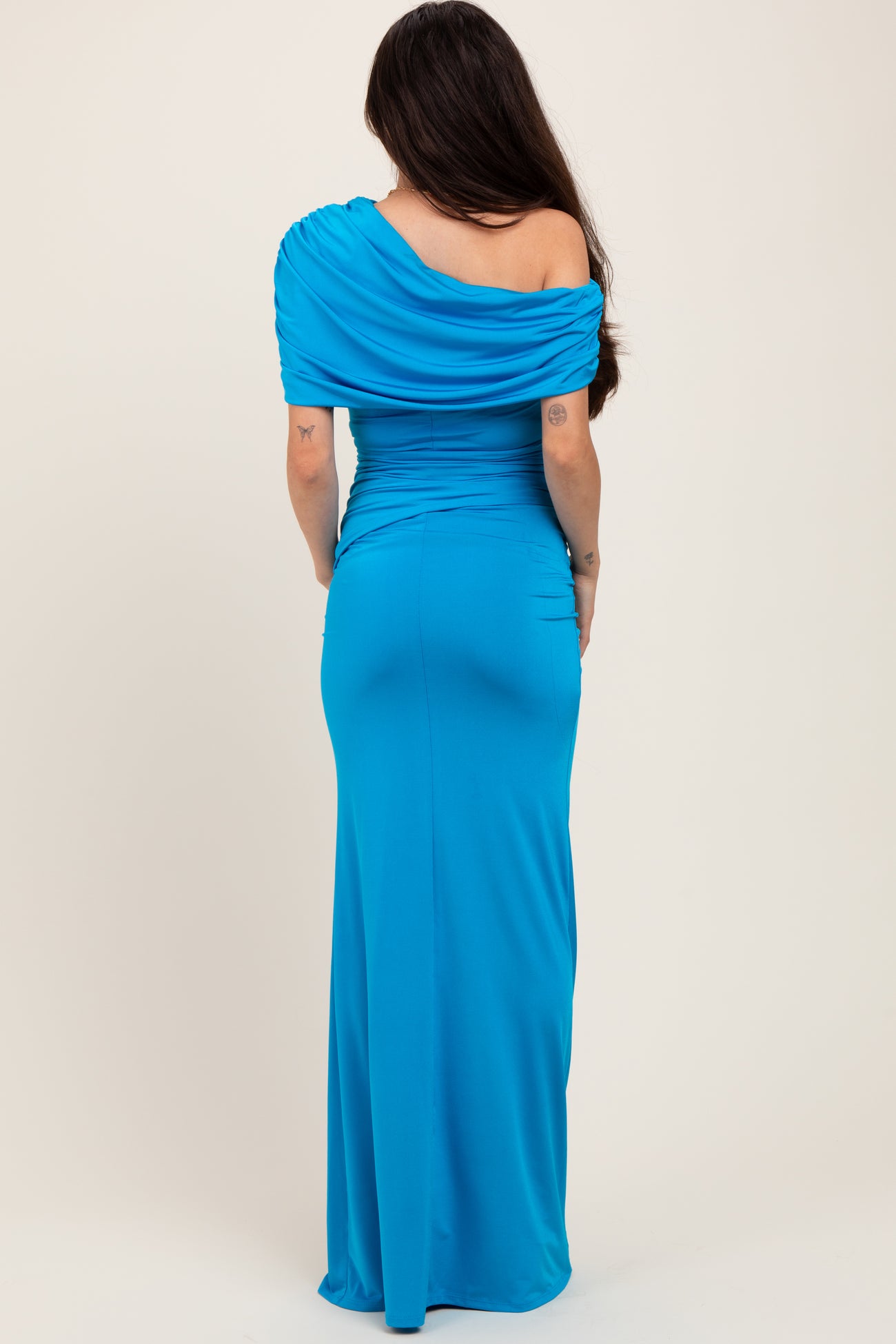 woman wearing a blue one-shoulder maternity dress with ruched detailing, showing a baby bump from the back