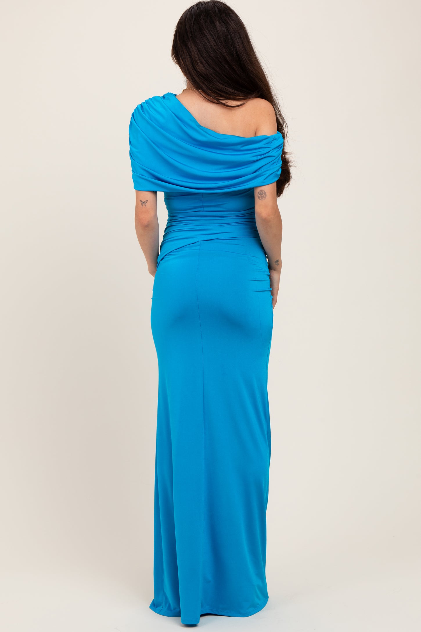 woman wearing a blue one-shoulder maternity dress with ruched detailing, showing a baby bump from the back