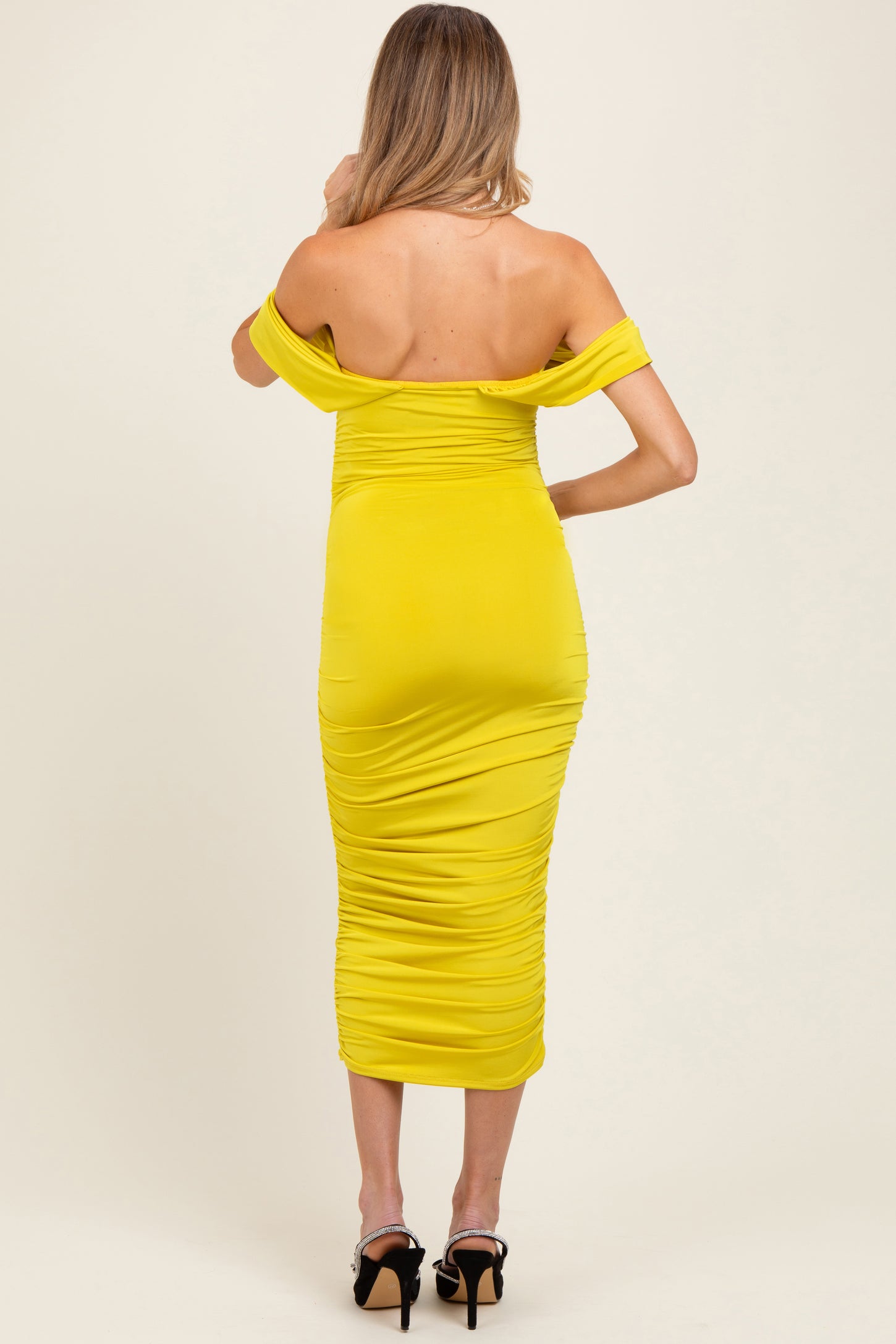 woman wearing a bright yellow off-the-shoulder maternity dress with ruched detailing, showing a fitted silhouette