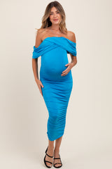 woman wearing a bright blue off-the-shoulder ruched maternity dress and holding her baby bump