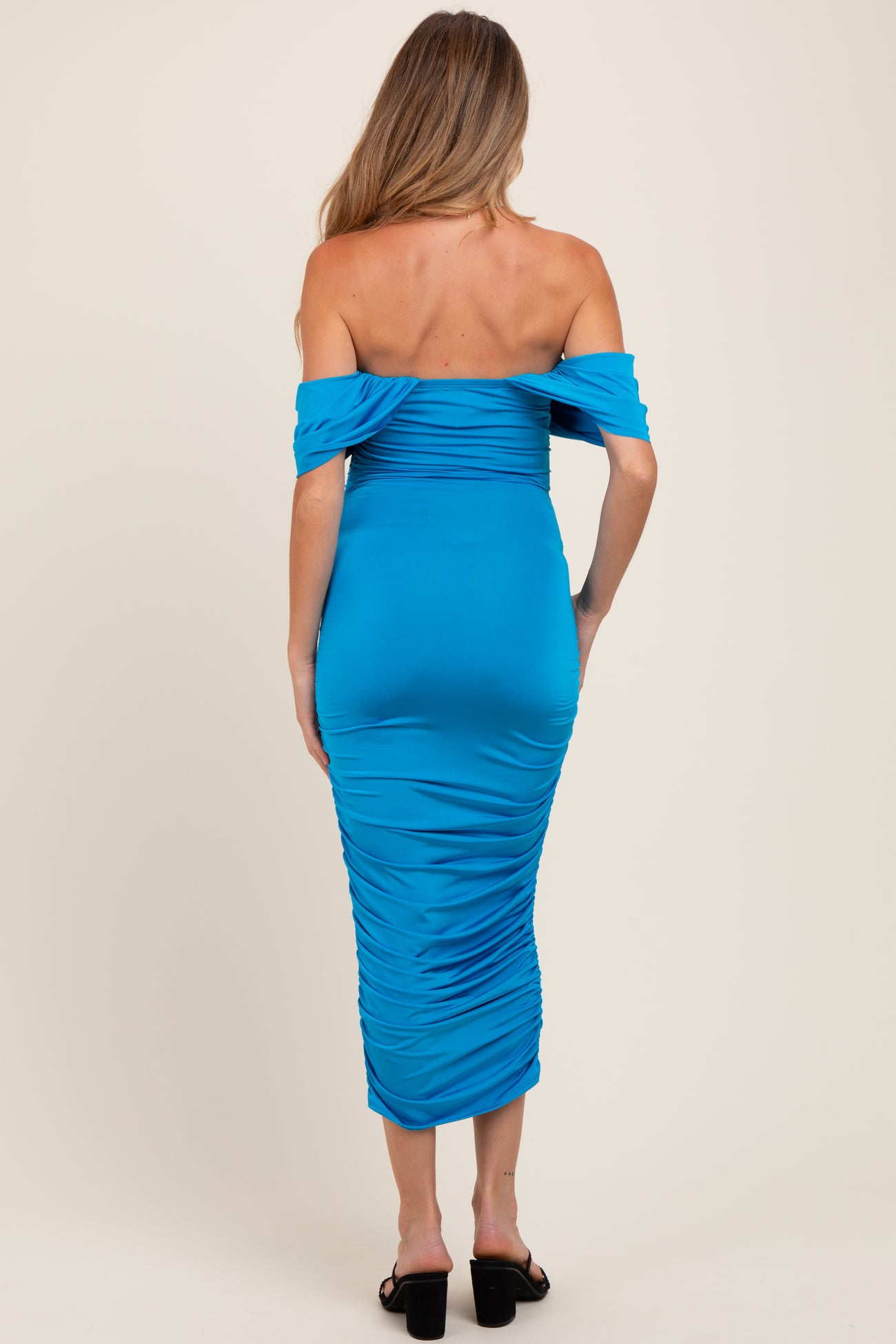 woman wearing a form-fitting turquoise off-the-shoulder maternity dress with ruching detail on the back