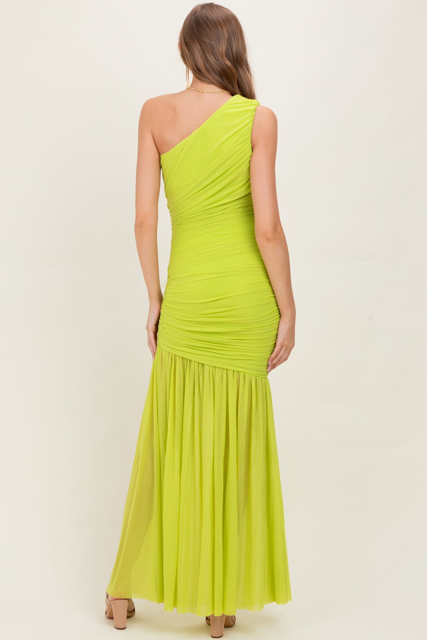 woman wearing a bright neon green one-shoulder maternity dress with ruched detailing and a flowing skirt