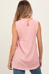 woman wearing a light pink sleeveless maternity top with a ruffled neckline and a keyhole back detail