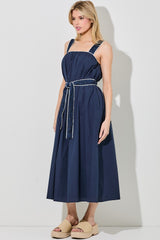woman wearing a navy blue sleeveless midi dress with a cinched waist and a matching belt, styled with beige platform sandals