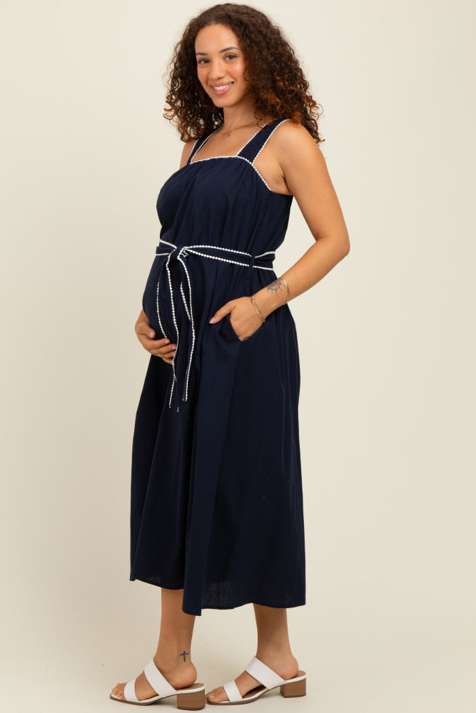 woman wearing a navy blue maternity dress with a belted waist and pockets, showing her baby bump