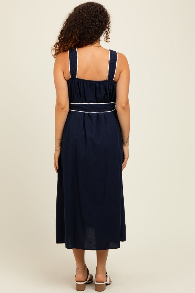 woman wearing a navy blue maternity maxi dress with adjustable straps and a cinched waist, showing her baby bump