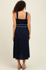 woman wearing a navy blue maternity maxi dress with adjustable straps and a cinched waist, showing her baby bump