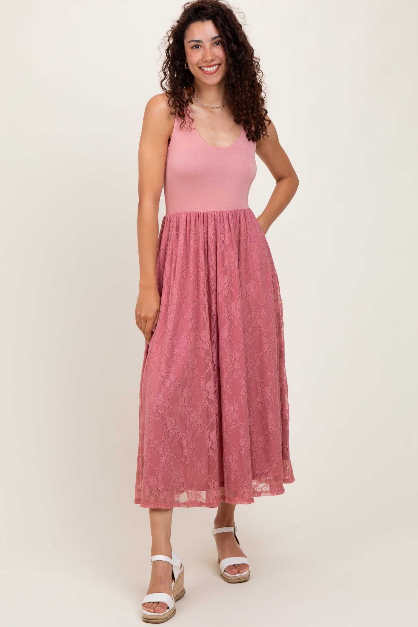 woman wearing a pink lace maxi dress with a fitted bodice and flared skirt, standing and smiling