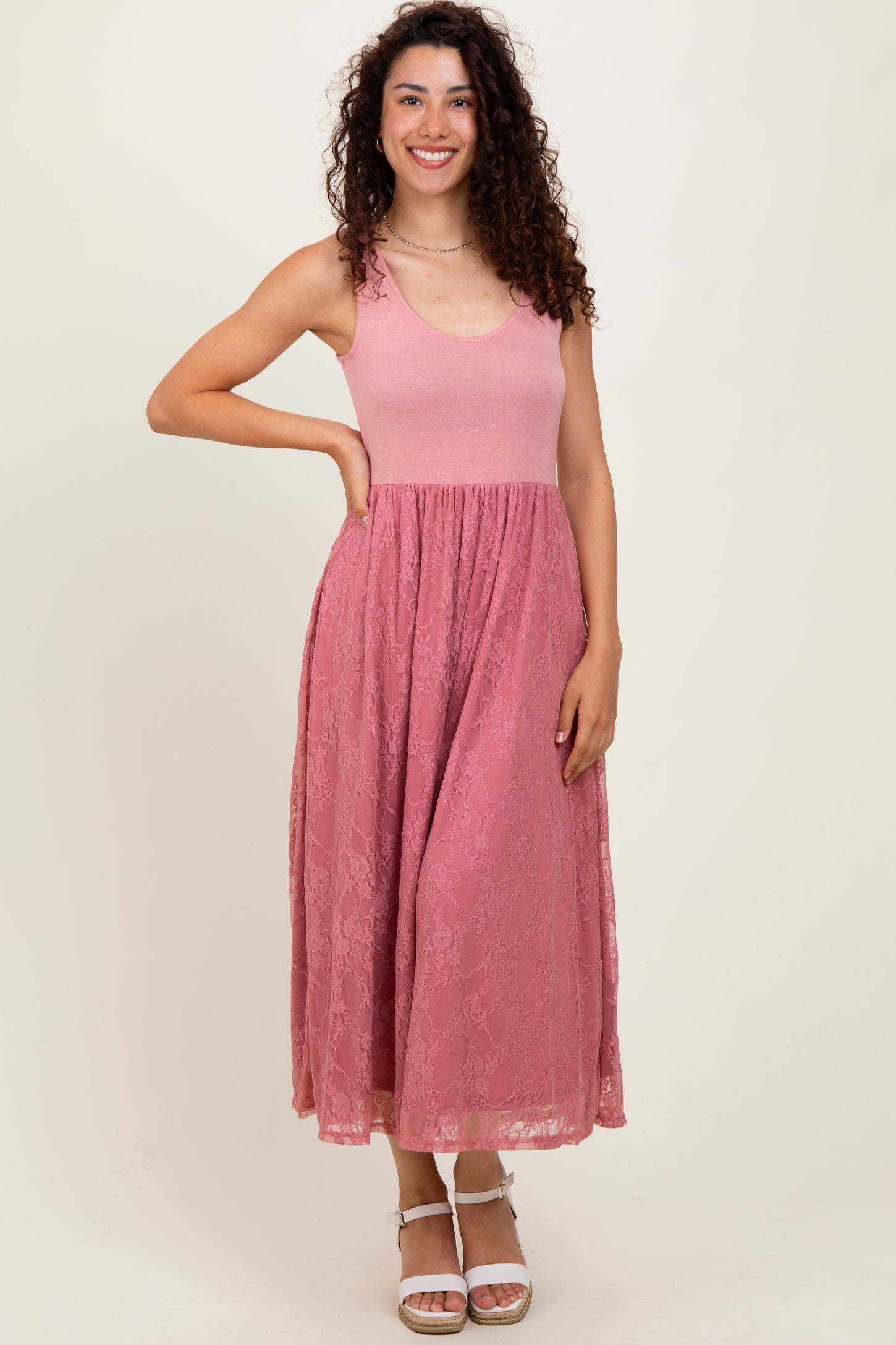 woman wearing a pink maxi dress with a fitted top and lace skirt, smiling and posing with one hand on her hip