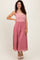 woman wearing a pink maxi dress with a fitted top and lace skirt, smiling and posing with one hand on her hip