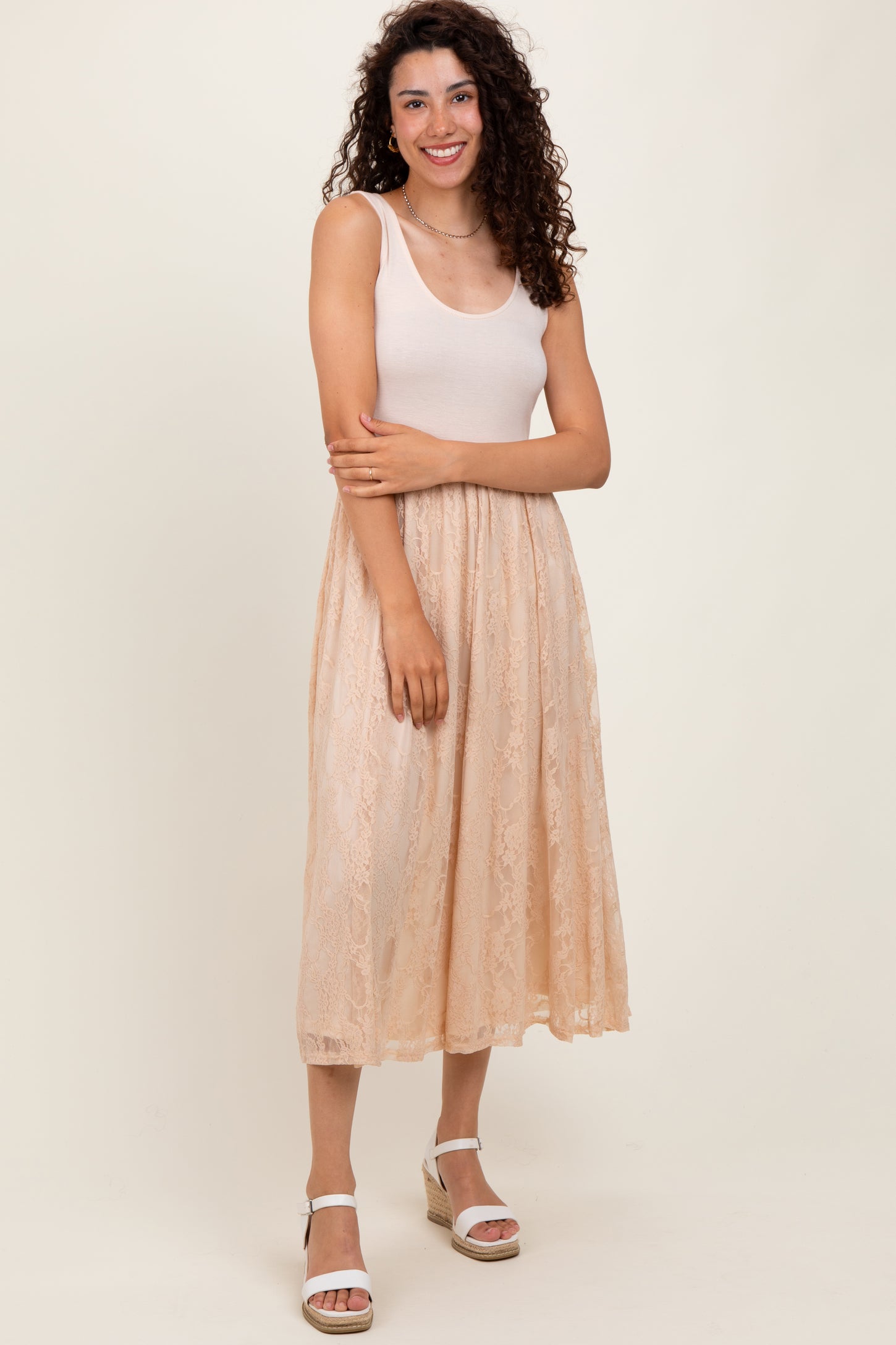 woman wearing a light pink tank top and a beige lace midi skirt with a flowy silhouette and standing in a natural pose