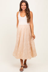 woman wearing a light pink maternity tank top with a flowy beige lace skirt and smiling at the camera