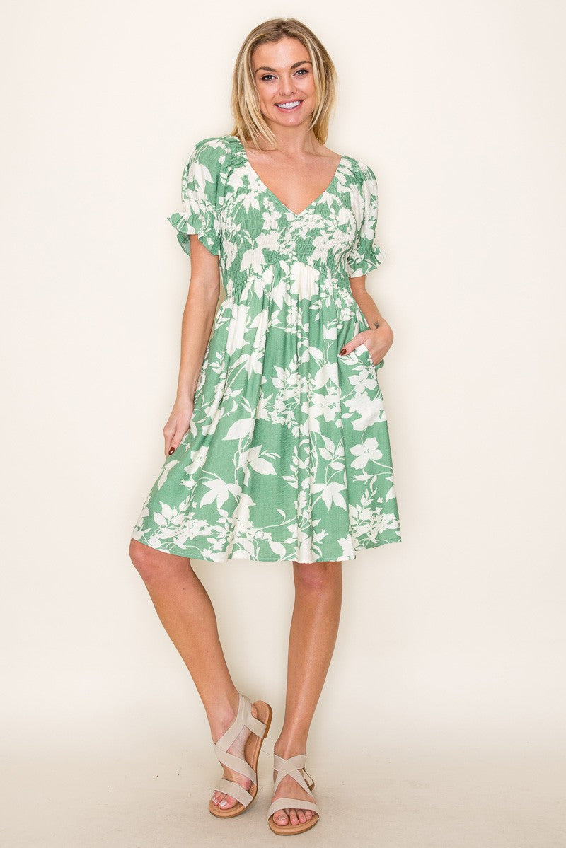 woman wearing a green floral print knee-length dress with short sleeves and pockets