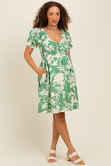 woman wearing a green floral maternity dress with short puff sleeves and pockets, showcasing a baby bump