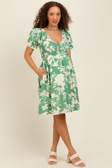 woman wearing a green floral maternity dress with short puff sleeves and pockets, showcasing a baby bump