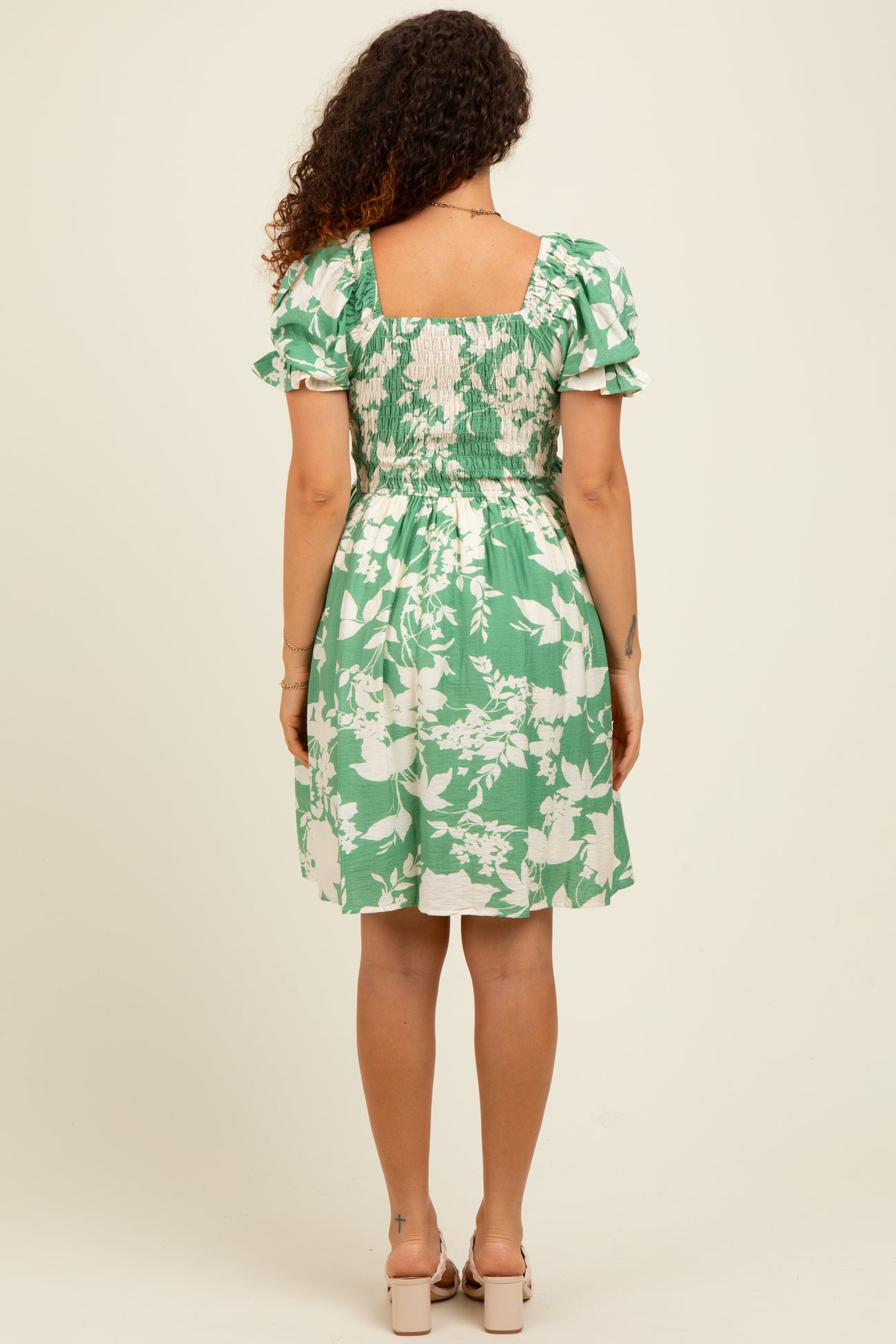 woman wearing a green floral maternity dress with puff sleeves and a smocked back, showcasing her baby bump