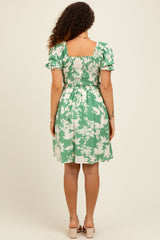 woman wearing a green floral maternity dress with puff sleeves and a smocked back, showcasing her baby bump