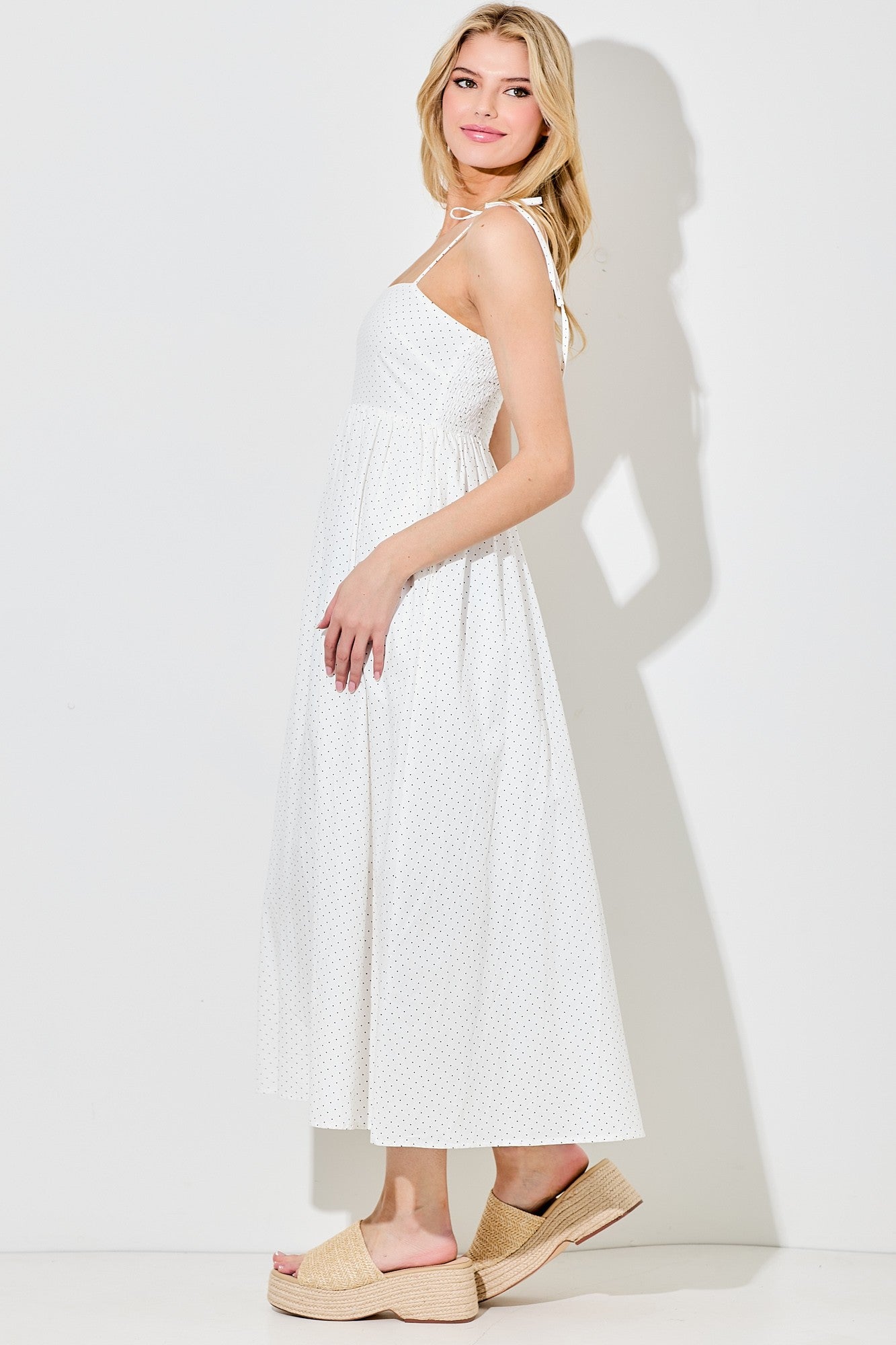 woman wearing a white polka dot maxi dress with a halter neck and flowy skirt, paired with tan wedge sandals