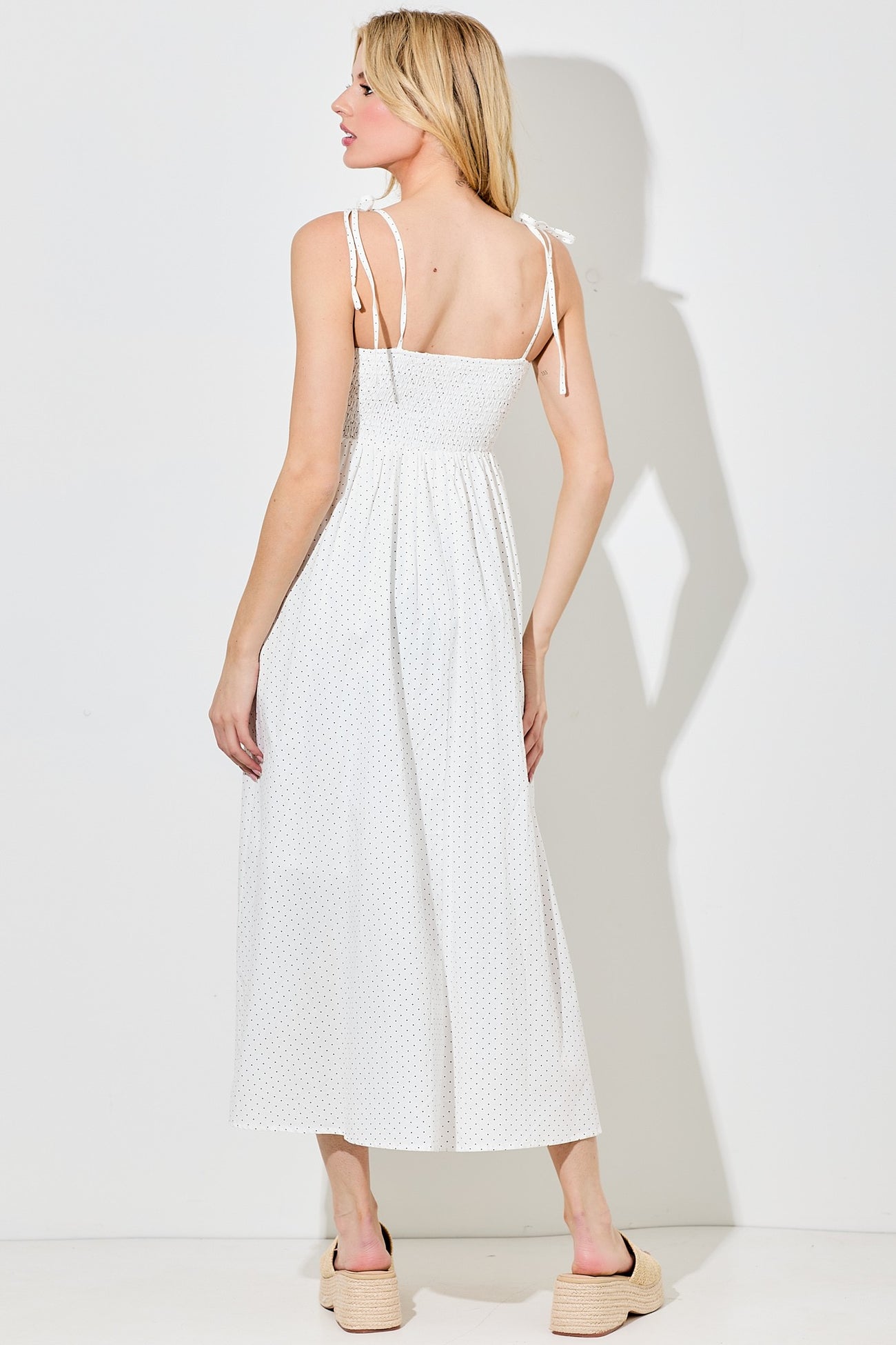 woman wearing a white polka dot maxi dress with tie straps, showing the back and a relaxed silhouette