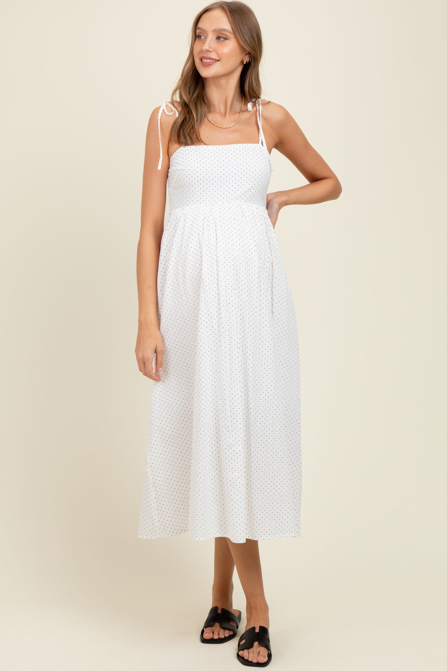 woman wearing a white polka dot maternity dress with spaghetti straps and a flowy skirt, showcasing her baby bump
