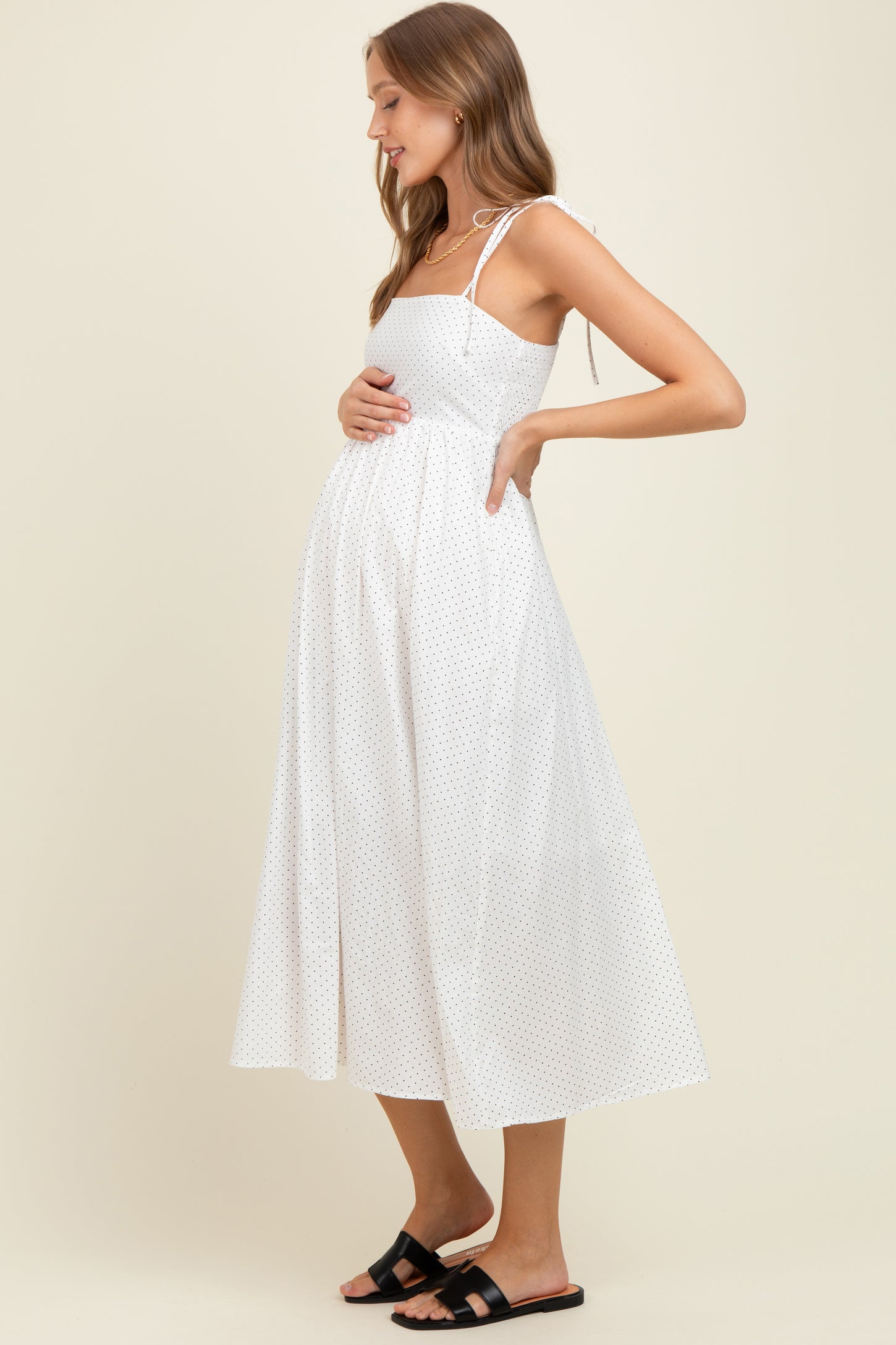 woman wearing a white polka dot maternity dress with tie straps and holding her baby bump