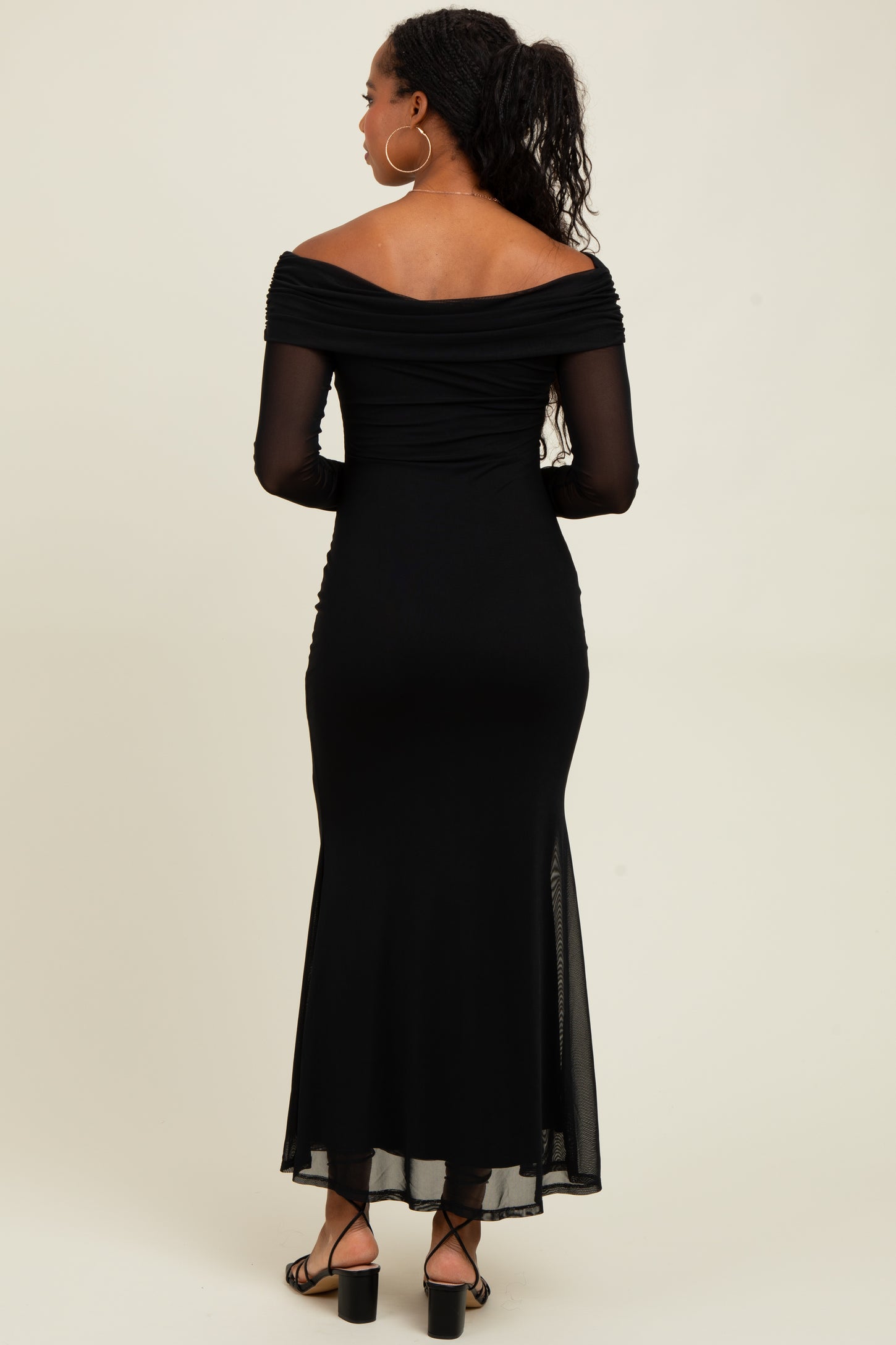 woman wearing a black off-the-shoulder fitted dress with sheer long sleeves and a flowy bottom, seen from the back