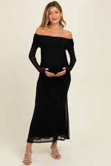 woman wearing a black off-the-shoulder maternity dress with long sheer sleeves and holding her baby bump