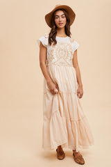 woman wearing a cream maxi dress with lace detailing and ruffle hem, paired with a wide-brimmed hat and brown flats
