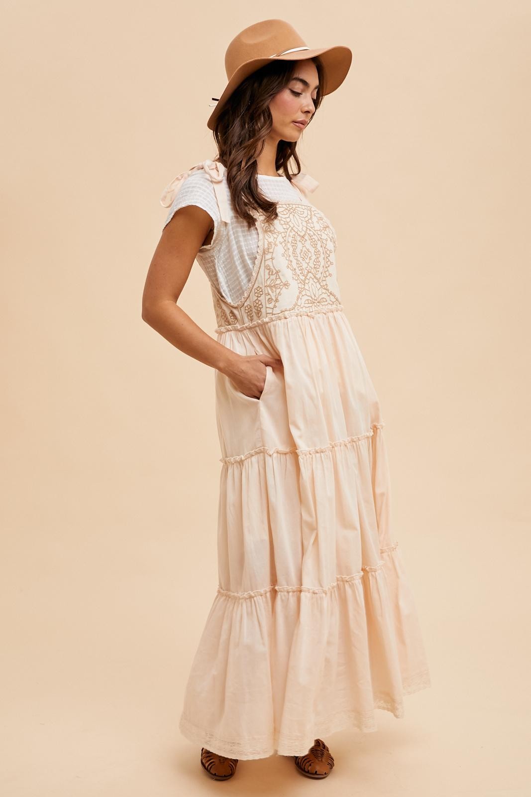 woman wearing a peach maxi dress with tiered layers and lace detailing, paired with a tan hat and a white t-shirt underneath