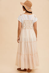 woman wearing a light beige tiered maxi dress with a lace-back detail and a tan wide-brim hat