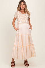 woman wearing a beige and peach tiered maxi maternity dress with embroidered details and pockets