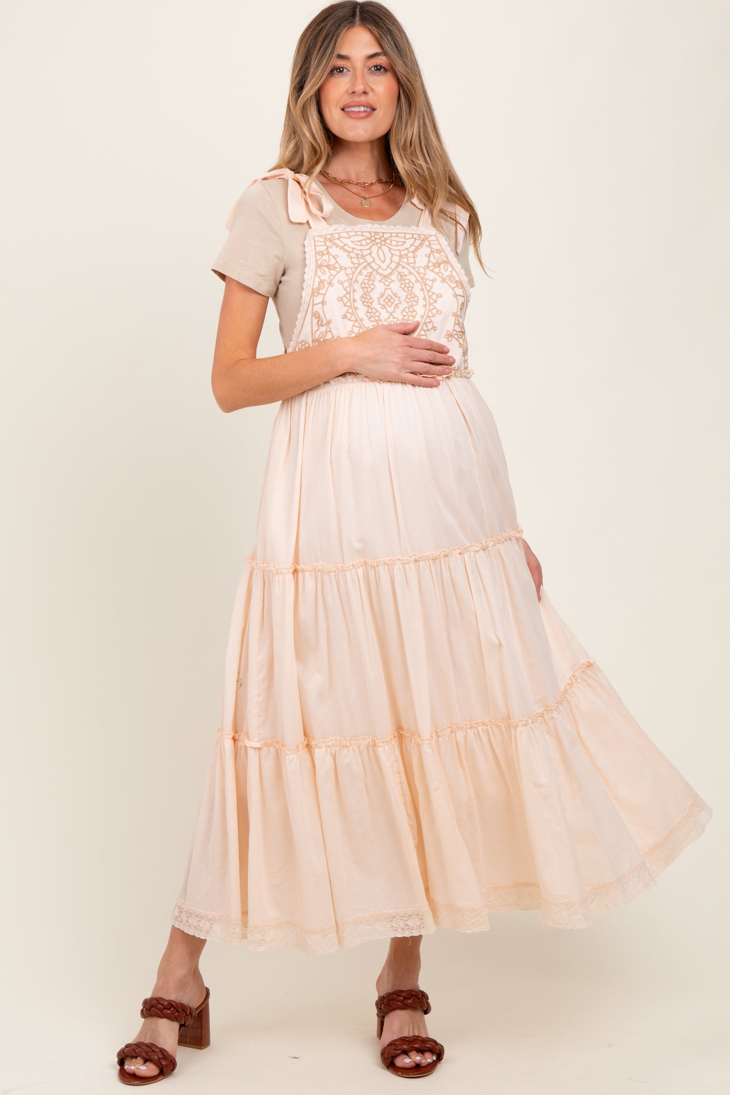 woman wearing a light peach maternity maxi dress with embroidery and a frill hem, showing her baby bump