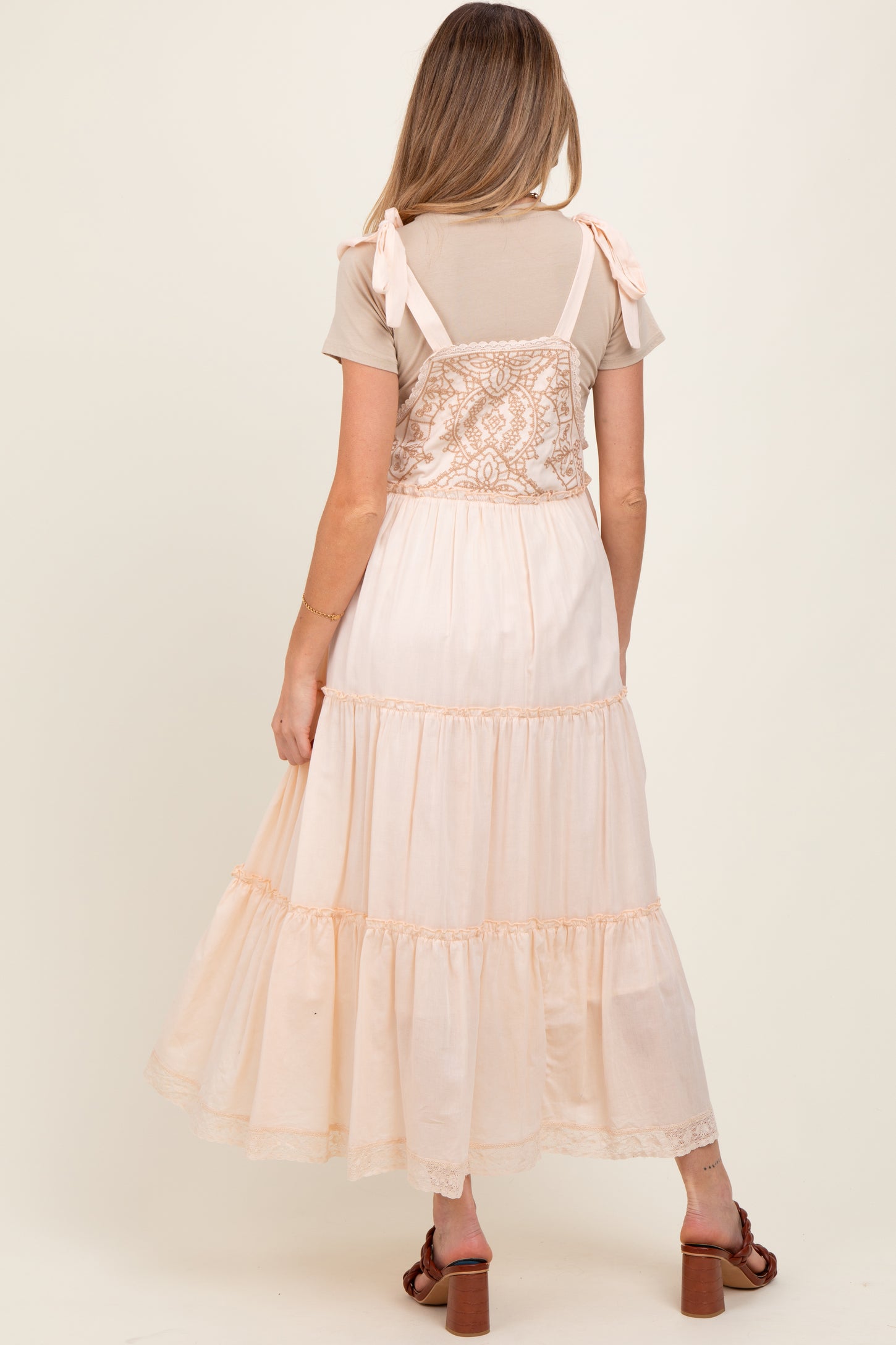 woman wearing a blush pink maternity dress with lace details and tiered ruffles, showing her baby bump from the back