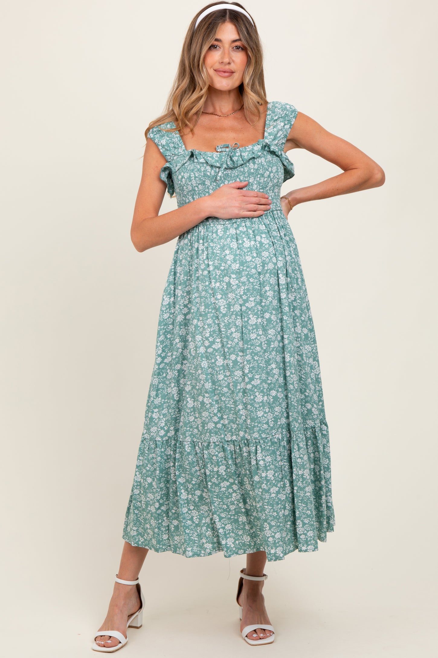 woman wearing a green floral maternity dress with ruffled sleeves and a tiered skirt, gently holding her baby bump